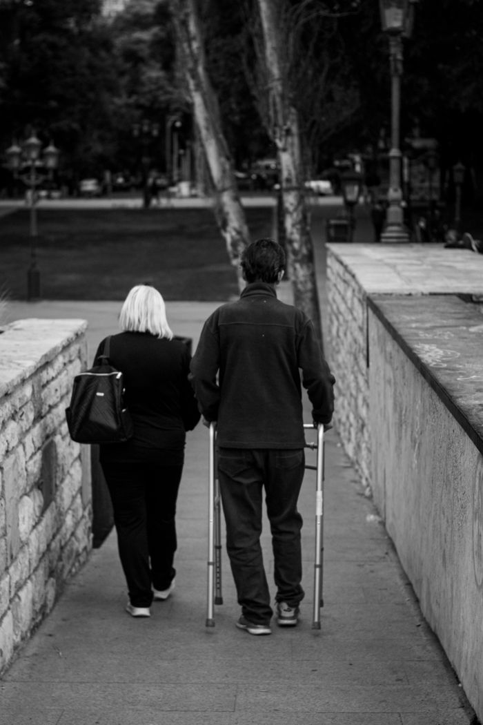 Services Black and white image of a couple walking with crutches in Mendoza park.